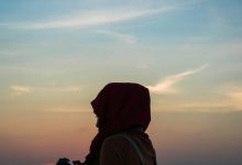woman holding DSLR camera near body of water